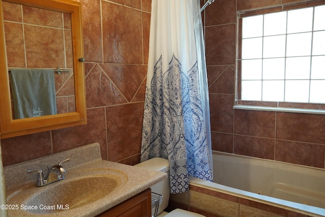 bathroom featuring toilet, shower / bathtub combination with curtain, vanity, and tile walls