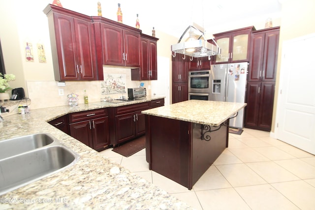 kitchen with reddish brown cabinets, appliances with stainless steel finishes, a kitchen island, and light stone counters