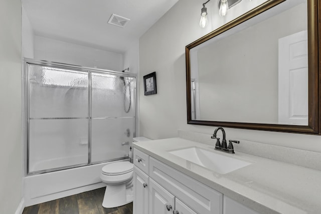 full bathroom with vanity, toilet, combined bath / shower with glass door, visible vents, and wood finished floors