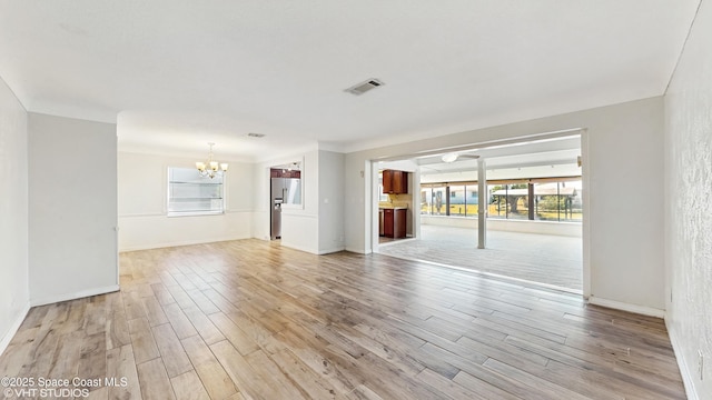 unfurnished living room with baseboards, visible vents, an inviting chandelier, and light wood-style flooring