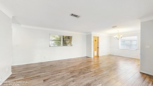 empty room featuring a chandelier, visible vents, light wood finished floors, and baseboards
