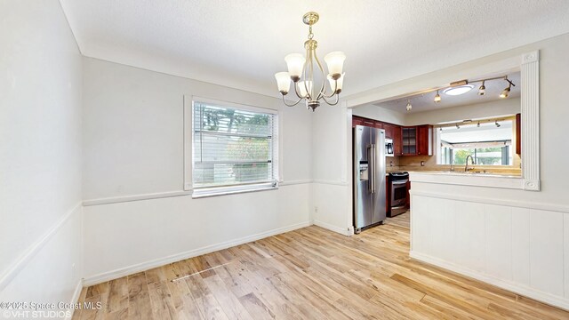 unfurnished dining area with a chandelier, a wealth of natural light, and light wood-style flooring