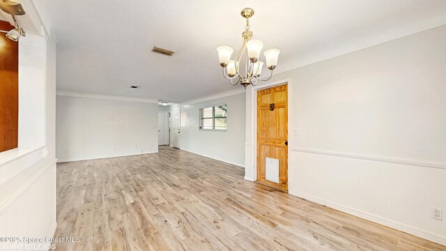 empty room featuring visible vents, baseboards, light wood finished floors, and a notable chandelier
