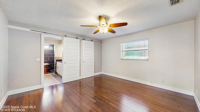unfurnished bedroom featuring a barn door, wood-type flooring, visible vents, baseboards, and a textured ceiling