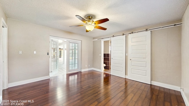 unfurnished bedroom with a textured ceiling, wood finished floors, and a barn door
