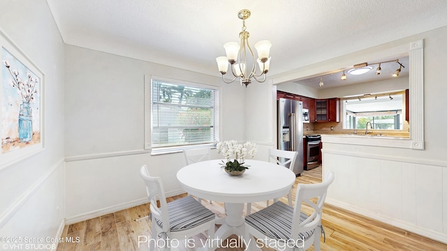 dining area featuring an inviting chandelier, a textured ceiling, light wood-style flooring, and wainscoting