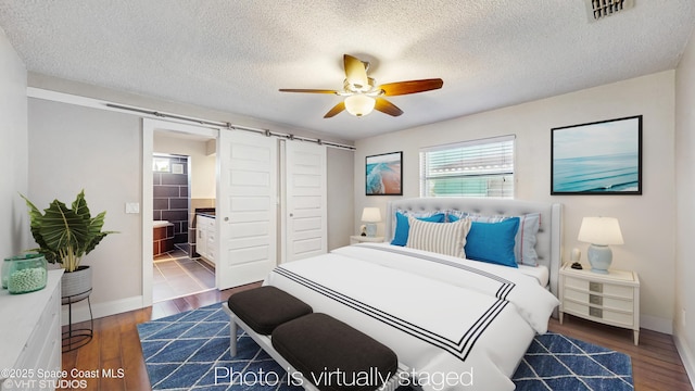 bedroom featuring wood finished floors, visible vents, baseboards, and a barn door