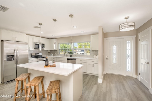 kitchen featuring stainless steel appliances, decorative backsplash, light wood-style flooring, and white cabinets