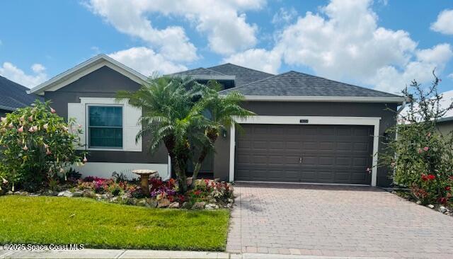 ranch-style home with stucco siding, decorative driveway, a garage, roof with shingles, and a front yard