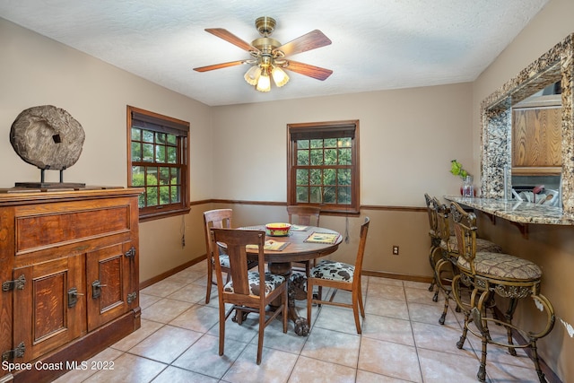 dining area featuring light tile patterned flooring, ceiling fan, a textured ceiling, and baseboards