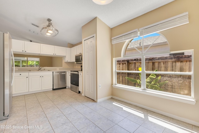 kitchen with a sink, light tile patterned flooring, light countertops, white cabinets, and appliances with stainless steel finishes