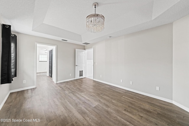 unfurnished living room featuring wood finished floors, a raised ceiling, a chandelier, baseboards, and a textured ceiling