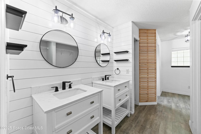 bathroom featuring wooden walls, wood finished floors, a textured ceiling, two vanities, and baseboards