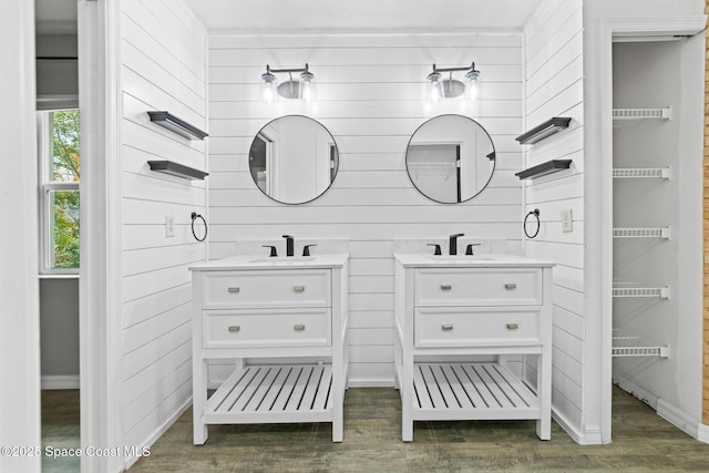 full bath with two vanities, wood finished floors, wooden walls, and baseboards
