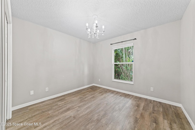 unfurnished room with a chandelier, wood finished floors, baseboards, and a textured ceiling