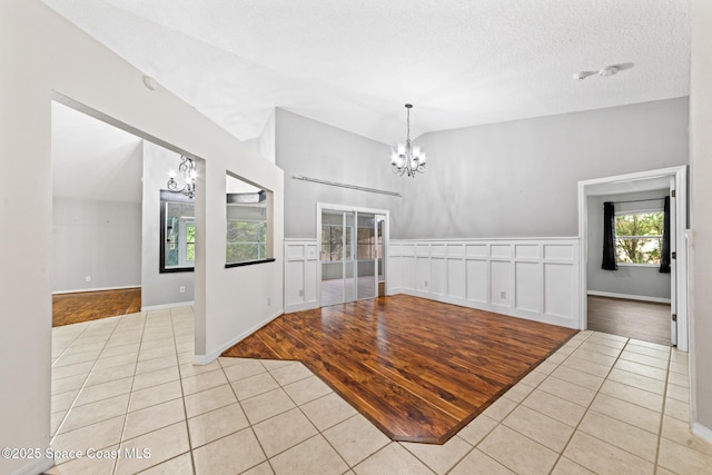 unfurnished dining area featuring a chandelier, tile patterned flooring, a textured ceiling, and vaulted ceiling