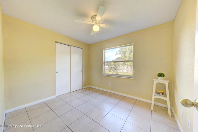 unfurnished bedroom featuring a closet, a ceiling fan, baseboards, and light tile patterned flooring