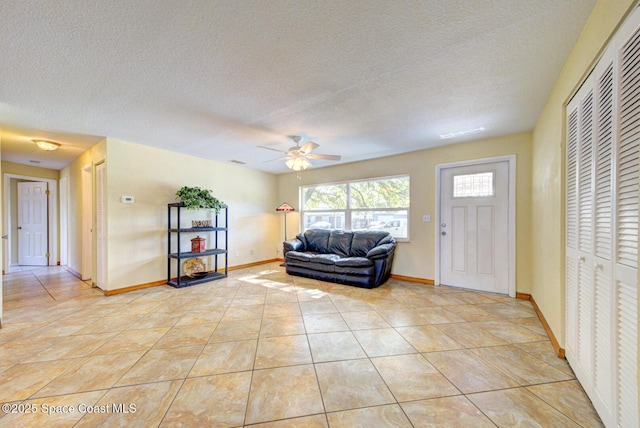 living room with light tile patterned floors, baseboards, a ceiling fan, and a textured ceiling