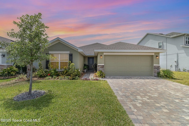 view of front of home featuring an attached garage, a front lawn, stone siding, stucco siding, and decorative driveway