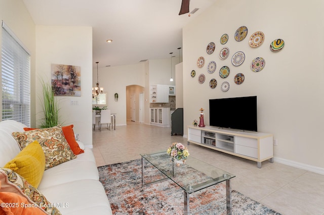 tiled living area featuring baseboards, arched walkways, ceiling fan with notable chandelier, and a towering ceiling