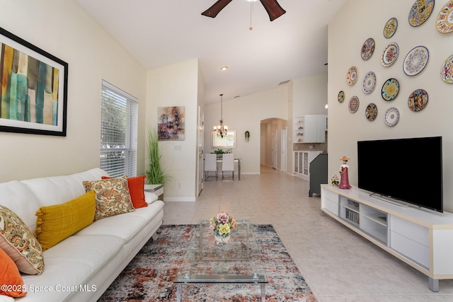 living room with light tile patterned floors, arched walkways, baseboards, high vaulted ceiling, and ceiling fan with notable chandelier