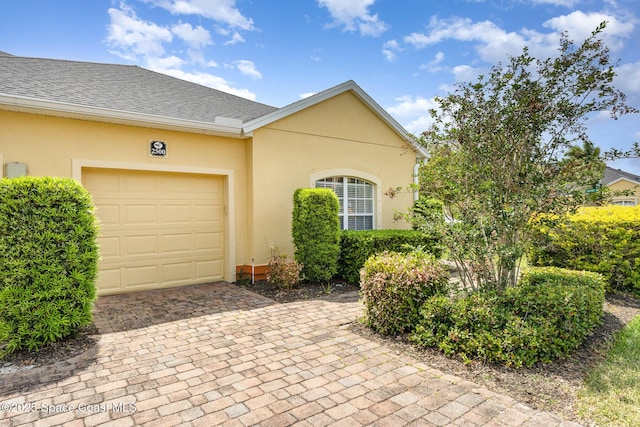 view of front of house with stucco siding, decorative driveway, roof with shingles, and a garage