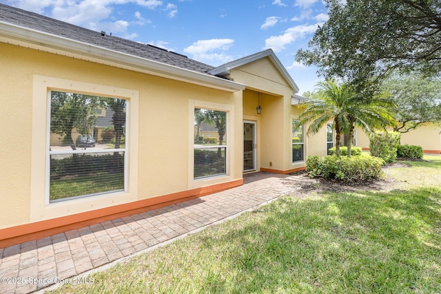 back of house featuring a yard, a shingled roof, stucco siding, and a patio area