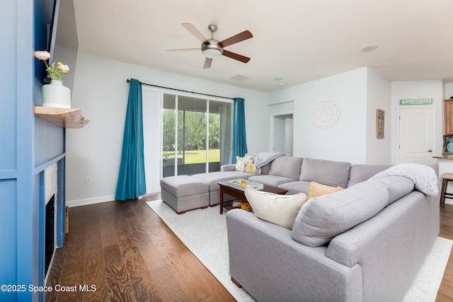 living room featuring visible vents, a fireplace, baseboards, ceiling fan, and dark wood finished floors