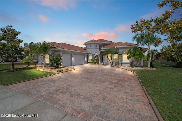 mediterranean / spanish home with an attached garage, a front lawn, stucco siding, decorative driveway, and a tiled roof