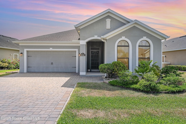 ranch-style home featuring a front lawn, stucco siding, decorative driveway, and an attached garage
