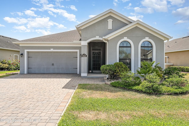 single story home with a front lawn, stucco siding, decorative driveway, and an attached garage