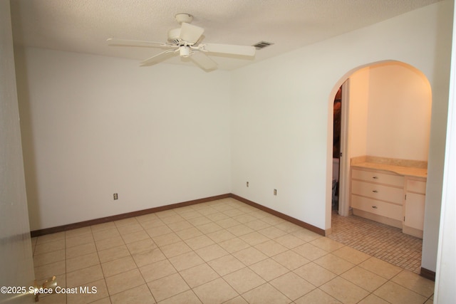 spare room featuring ceiling fan, visible vents, a textured ceiling, baseboards, and arched walkways