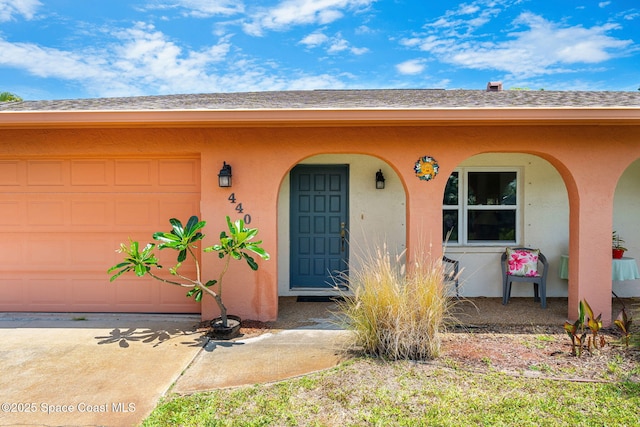 property entrance featuring stucco siding, an attached garage, and driveway