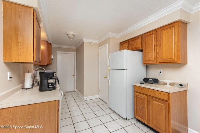 kitchen with brown cabinets, light countertops, freestanding refrigerator, ornamental molding, and light tile patterned flooring