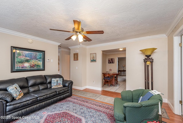 living room featuring a textured ceiling, ceiling fan, ornamental molding, and light wood-style flooring