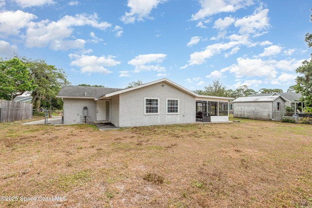rear view of property with a gate, a sunroom, a fenced backyard, a yard, and stucco siding