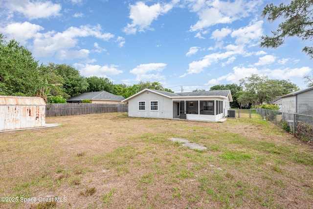back of house featuring a yard, an outdoor structure, a fenced backyard, and a sunroom