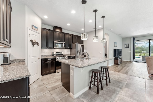 kitchen with a sink, a textured ceiling, stainless steel appliances, open floor plan, and tasteful backsplash