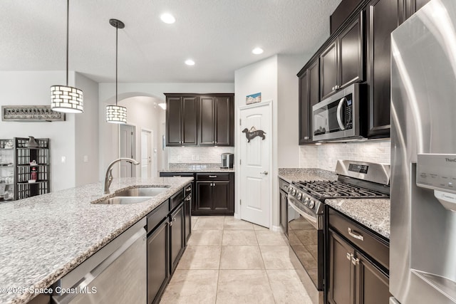 kitchen featuring a sink, arched walkways, stainless steel appliances, backsplash, and pendant lighting