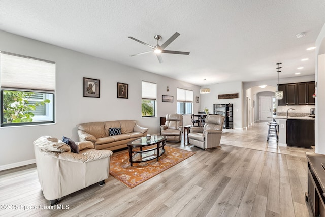 living area with baseboards, ceiling fan, a textured ceiling, arched walkways, and light wood-style flooring