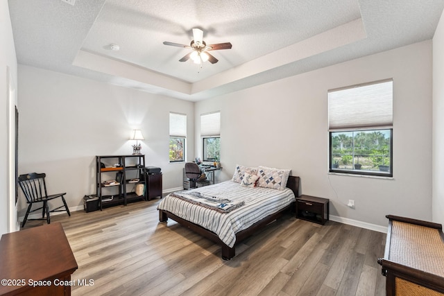 bedroom featuring baseboards, a tray ceiling, multiple windows, and light wood-style flooring