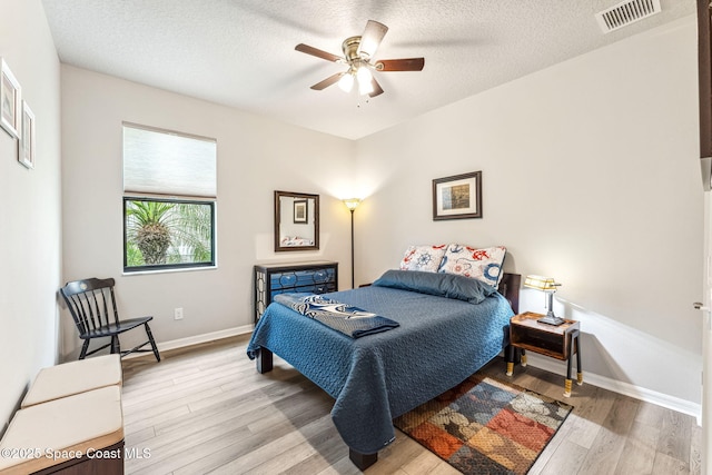 bedroom with a ceiling fan, a textured ceiling, visible vents, wood finished floors, and baseboards