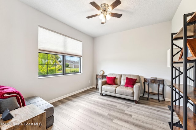 living area with a textured ceiling, baseboards, a ceiling fan, and wood finished floors