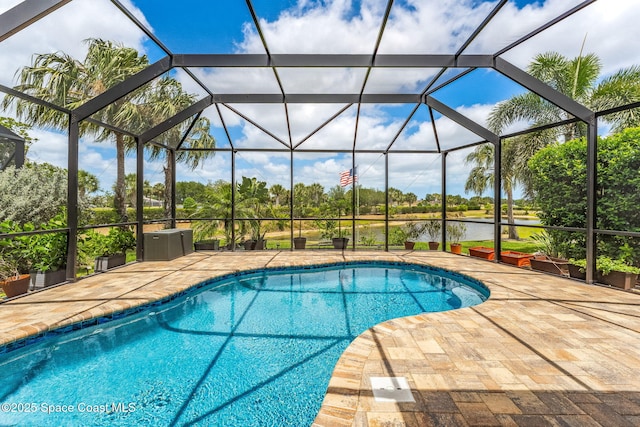 outdoor pool with glass enclosure, a patio, and a water view