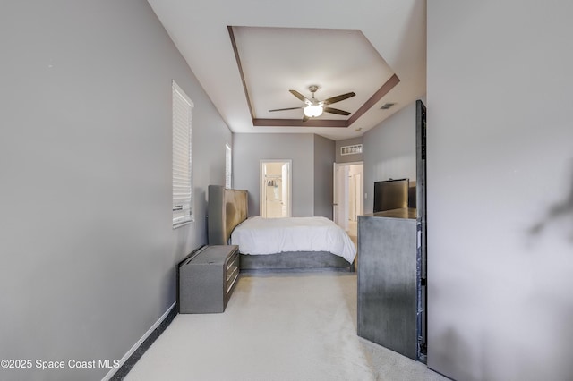 bedroom featuring visible vents, baseboards, ensuite bathroom, ceiling fan, and a tray ceiling