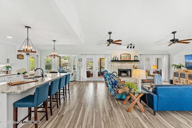320 Amberjack Pl, Melbourne Beach, FL 32951 - living area featuring french doors, ceiling fan with notable chandelier, light wood-type flooring, and a stone fireplace