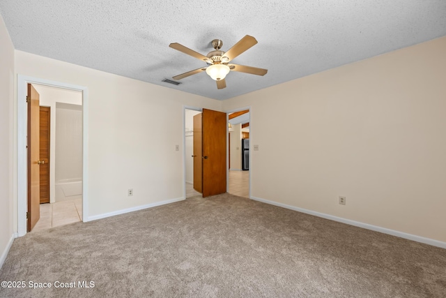 unfurnished bedroom featuring ensuite bath, visible vents, light carpet, baseboards, and a textured ceiling