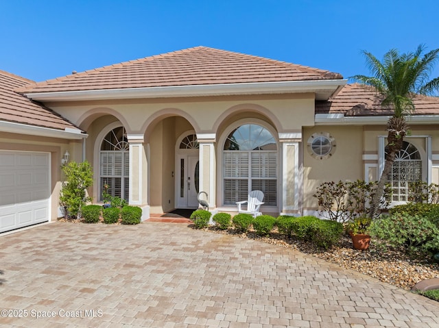 property entrance featuring covered porch, decorative driveway, stucco siding, a tiled roof, and an attached garage