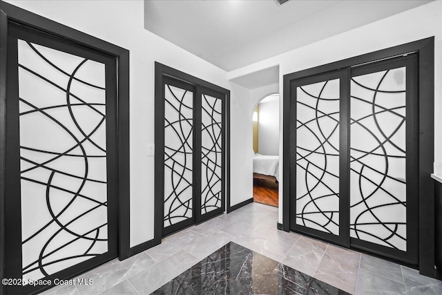 entryway featuring baseboards, marble finish floor, and arched walkways
