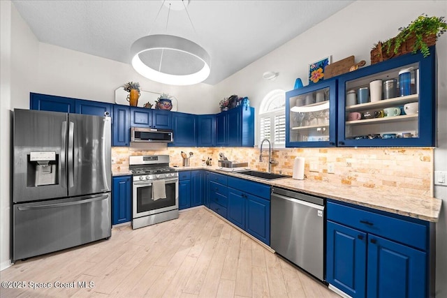 kitchen featuring glass insert cabinets, a sink, stainless steel appliances, blue cabinetry, and light wood finished floors